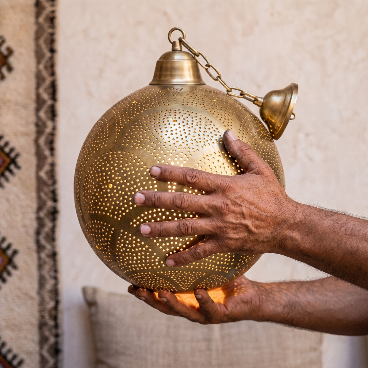 Artisan's hands holding the pierced brass body of the Tanirt pendant