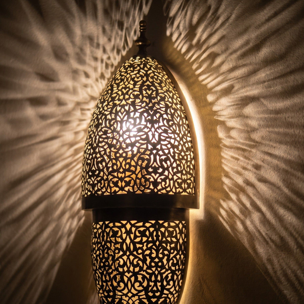 Close view of the lit Tarz sconce, filigree piercing glowing like stitches of light