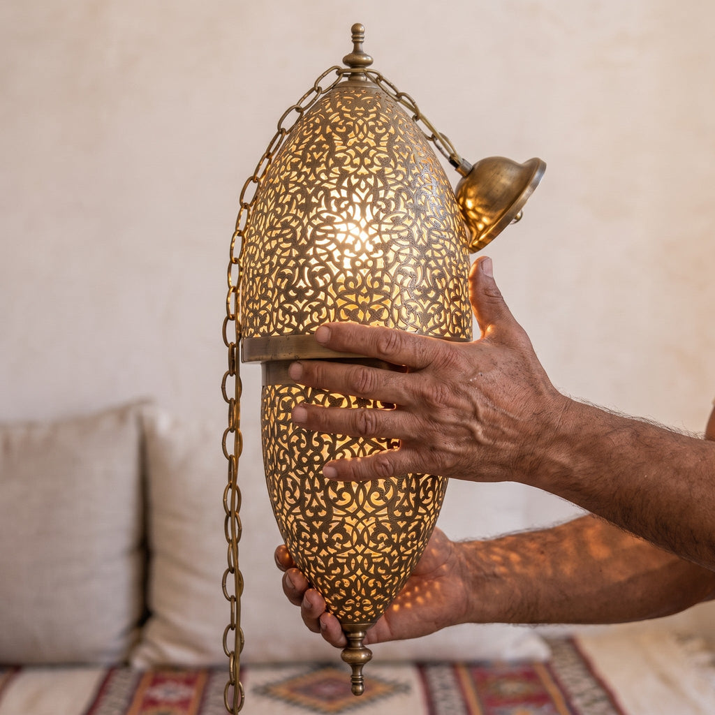 A maalem's hands holding the pierced brass body of the Tarz sconce