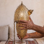 A maalem's hands holding the pierced brass body of the Tarz sconce