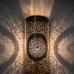 Lit Tislit sconce up close, light passing through the hand-pierced brass pattern