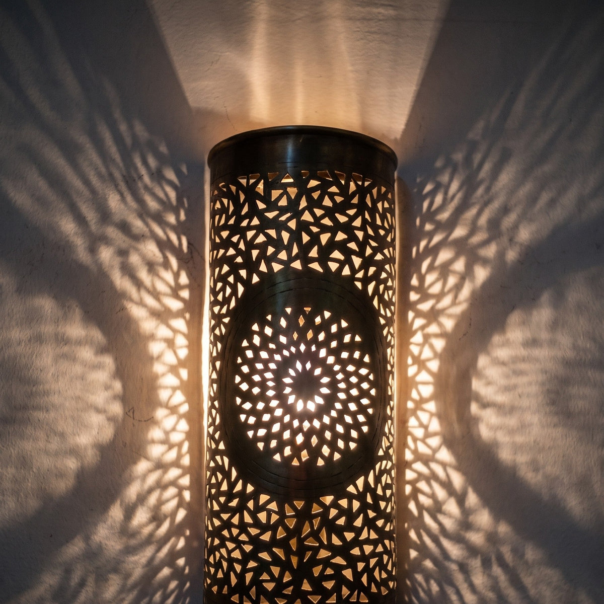 Lit Tislit sconce up close, light passing through the hand-pierced brass pattern