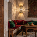 Two Tislit sconces glowing against a plaster wall in a Moroccan riad at dusk
