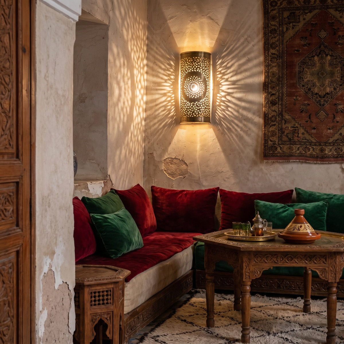 Two Tislit sconces glowing against a plaster wall in a Moroccan riad at dusk