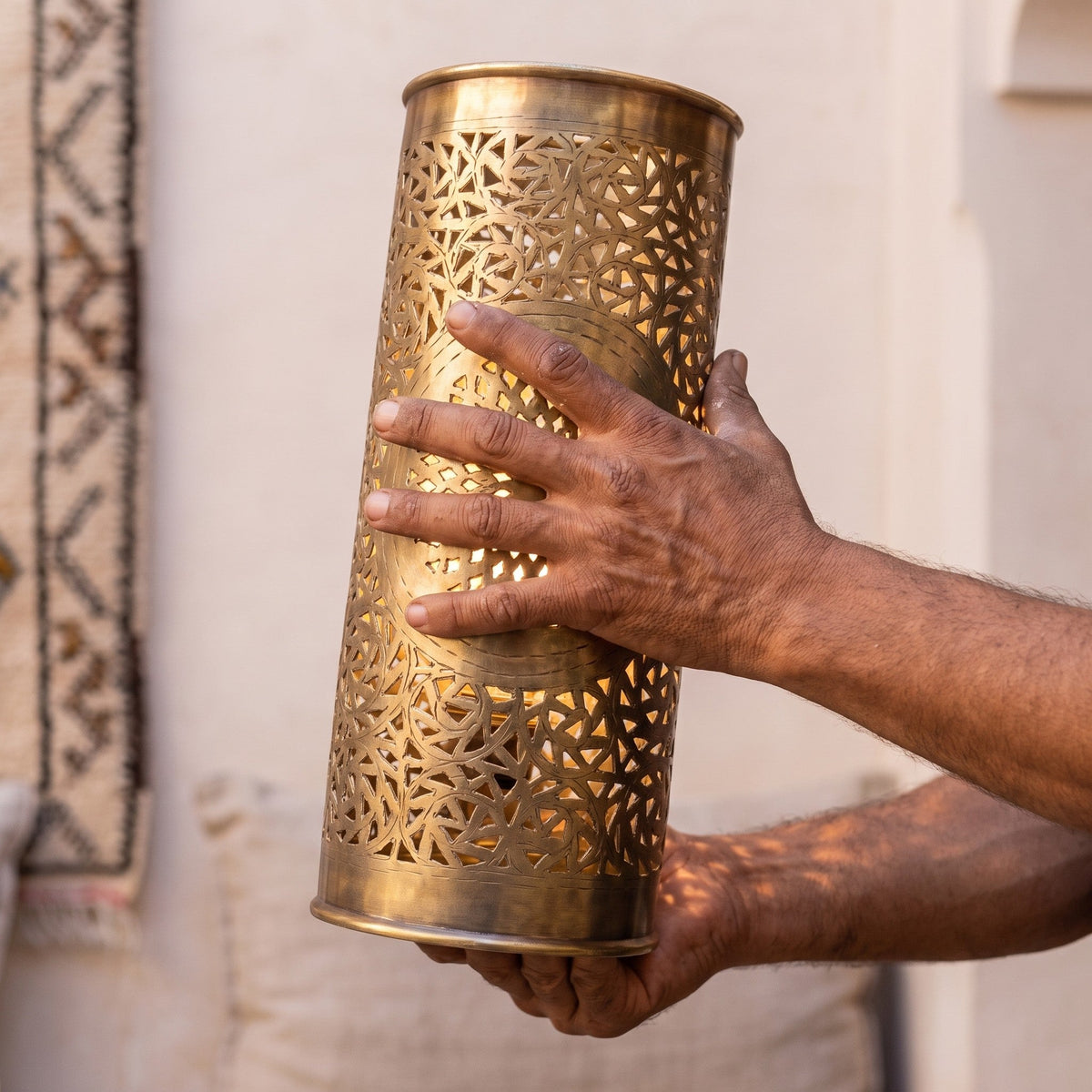 A maker's hands holding one pierced brass Tislit sconce shade in the workshop