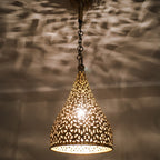 Close detail of the lit Tizi pendant, floral cutwork glowing in the brass