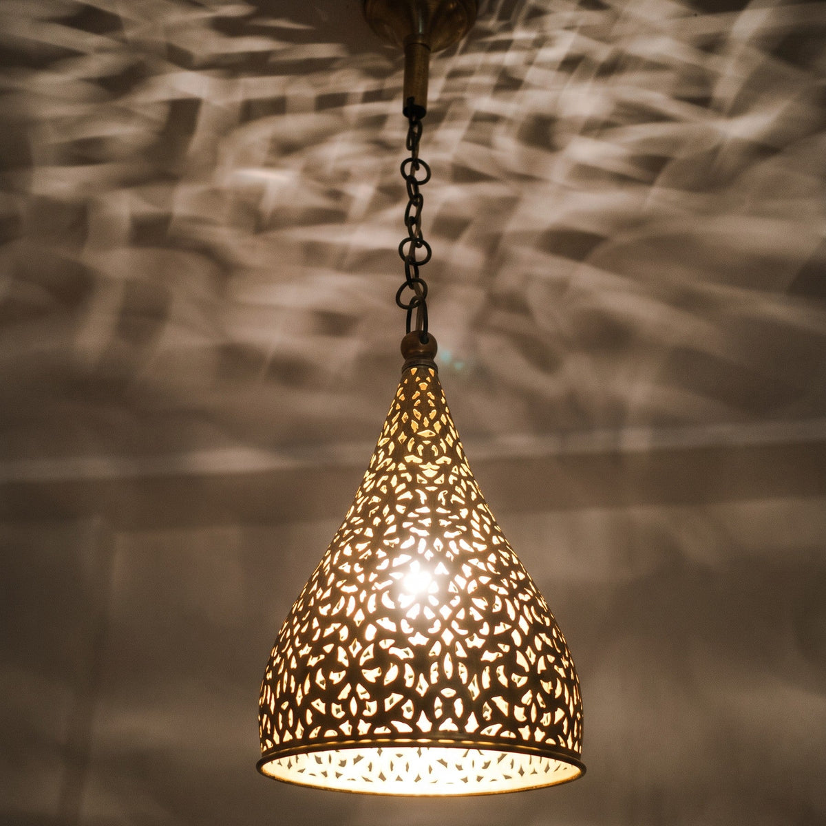 Close detail of the lit Tizi pendant, floral cutwork glowing in the brass