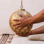 Maker's hands holding the pierced brass shade of the Tiziri pendant