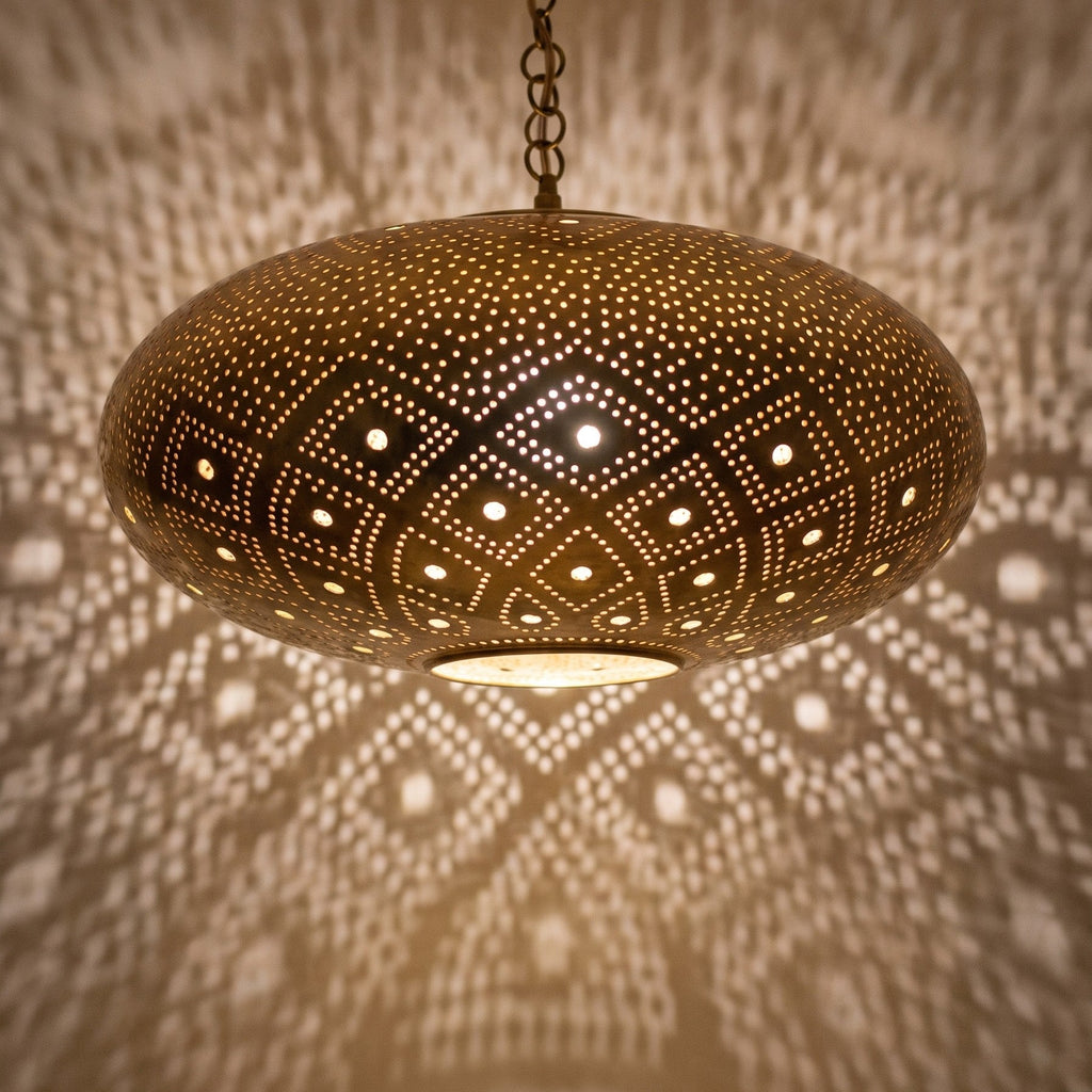 Close-up of the Tudert pendant lit, openings glowing in the brass