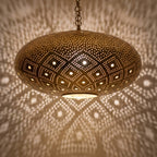 Close-up of the Tudert pendant lit, openings glowing in the brass