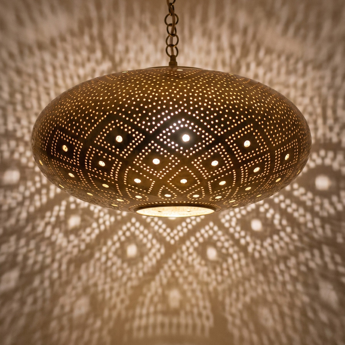 Close-up of the Tudert pendant lit, openings glowing in the brass