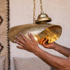Maker's hands holding the hammered brass shade of the Warqa pendant