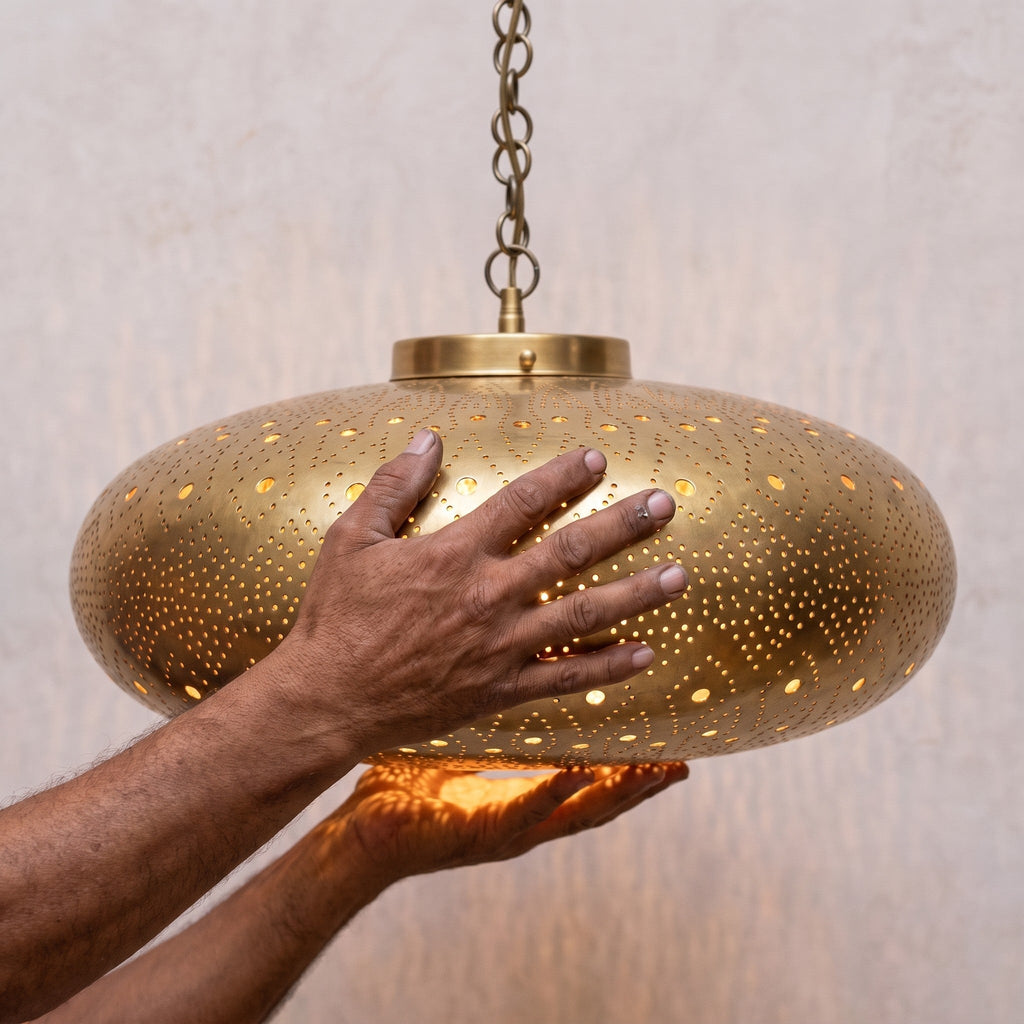 A maker's hands holding the pierced brass shade of the Yakout pendant