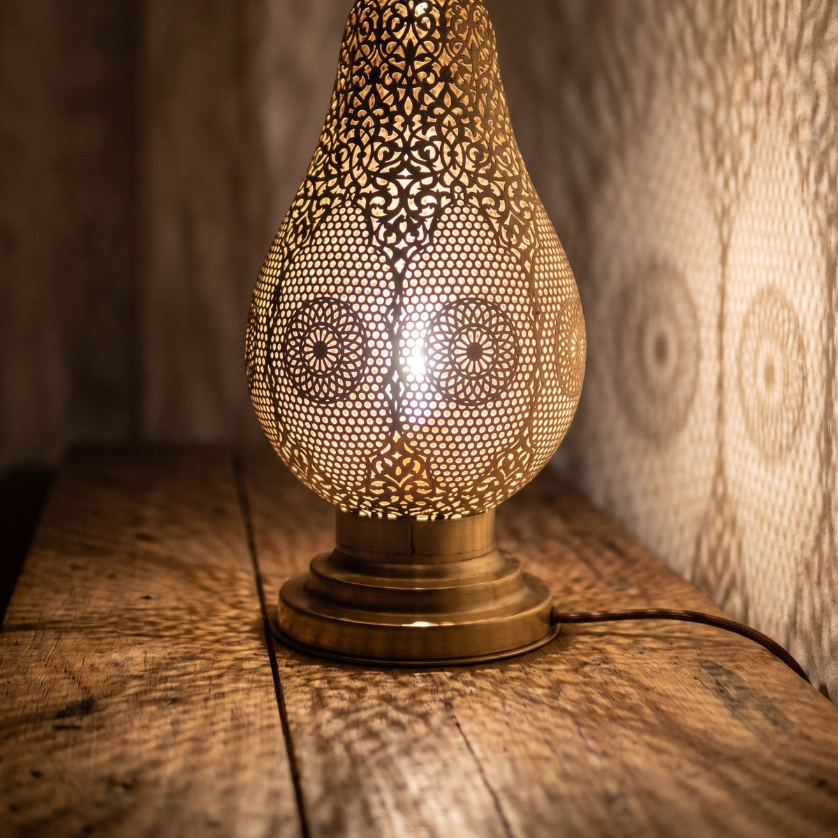 Close detail of the lit Zina lamp, light coming through the hand-pierced brass openings