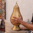 A maalem holds the pierced brass shade of the Zina lamp in his hands at the workshop