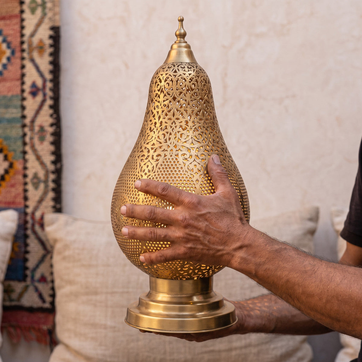 A maalem holds the pierced brass shade of the Zina lamp in his hands at the workshop
