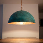 Close detail of the lit Zitoun pendant, copper interior glowing under the verdigris rim