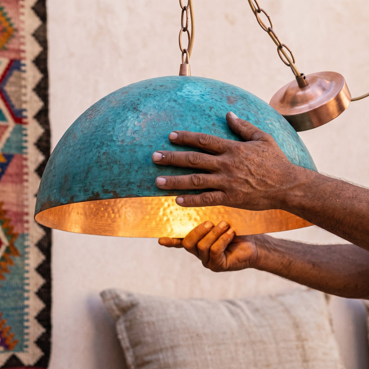 Artisan's hands holding the oxidized green dome of the Zitoun pendant